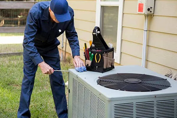 Technician working on a residential outdoor air conditioner beside a house
